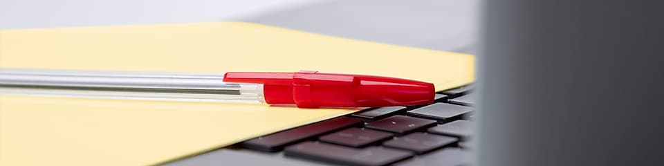 Roter Kugelschreiber und gelbes Blatt Papier auf der  Tastatur eines Laptops